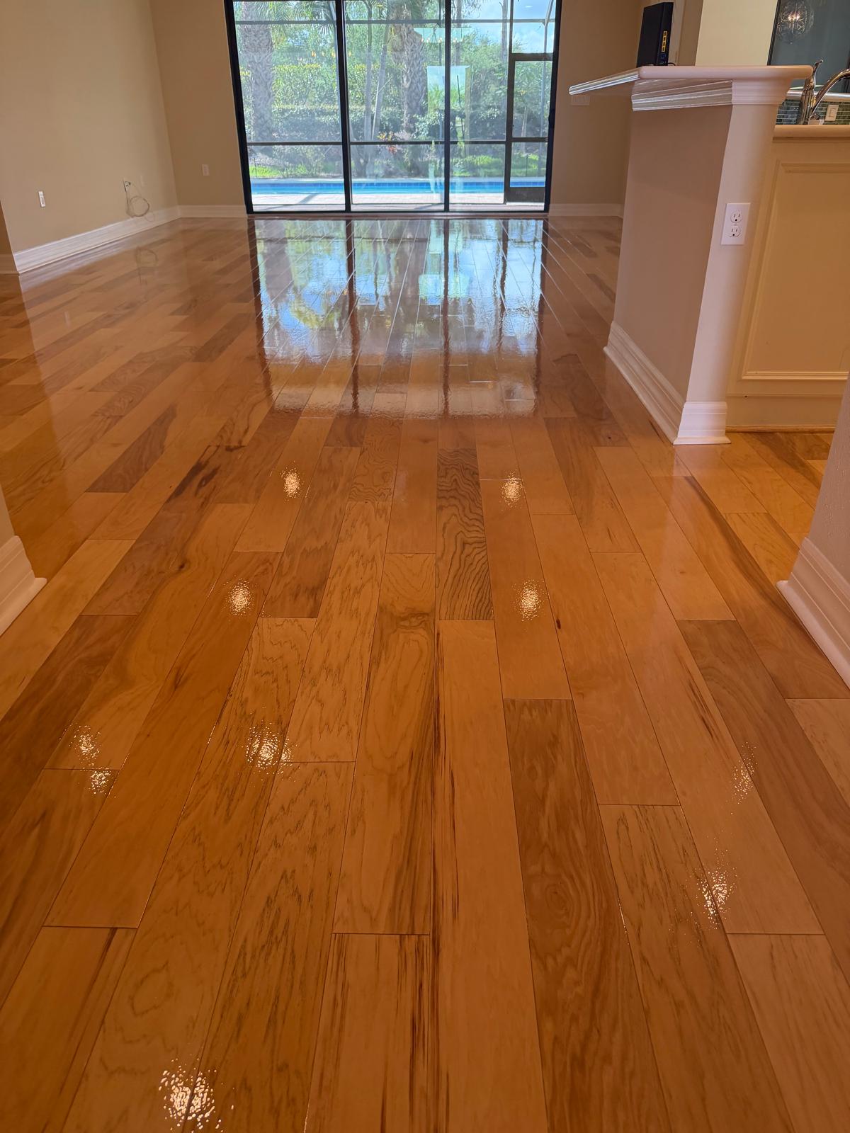 A bright living room with glossy honey-toned hardwood flooring and glass doors leading to a pool